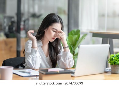 Young Asian woman feeling migraine head strain. Tired, Overworked businesswoman financier while working on laptop computer in office. - Shutterstock ID 2074735093