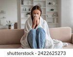 Young asian woman feeling unwell at home, sneezing into tissue, sick korean female sitting wrapped in cozy blanket on couch in living room, millennial lady suffering from cold, copy space