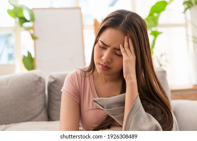 Young Asian woman feeling unwell and have a headache while sitting on the sofa