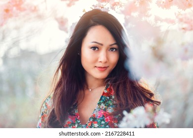 Young Asian woman, in a floral pattern dress, in front of blossoming cherry tree in the spring time . High quality photo