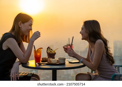 Young Asian Woman Friends Celebrating Dinner Party Meeting At Skyscraper Rooftop Restaurant Bar In Metropolis At Summer Sunset. Beautiful Girl Enjoy Outdoor Lifestyle Together On Holiday Vacation.