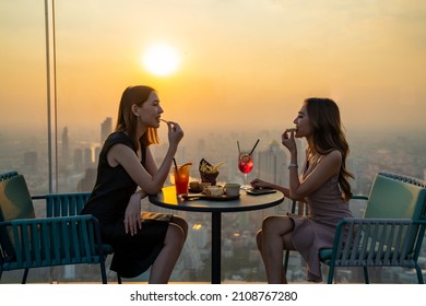 Young Asian Woman Friends Celebrating Dinner Party Meeting At Skyscraper Rooftop Restaurant Bar In Metropolis At Summer Sunset. Beautiful Girl Enjoy Outdoor Lifestyle Together On Holiday Vacation.