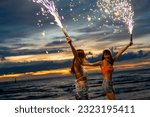 Young Asian woman friends playing sparklers firework together at tropical island beach at summer sunset. Attractive girl enjoy and fun outdoor lifestyle beach party on holiday travel vacation.