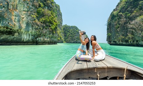 Young Asian woman friends using mobile phone taking selfie together while travel on boat passing island beach lagoon in sunny day. Happy female enjoy and fun outdoor lifestyle on summer vacation trip