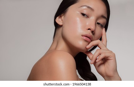 Young asian woman with glowing skin looking away with an attitude. Female with beautiful skin against beige background.
