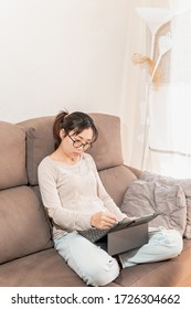 Young asian woman graphic designer drawing on an ipad tablet. Girl working from home sitting on the sofa couch. Work from home due to coronavirus pandemic.