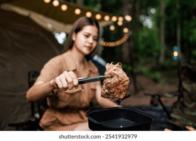 Young asian woman grilling meat on a portable gas stove while camping in nature park at evening time. Travel, adventure and vacation concept - Powered by Shutterstock