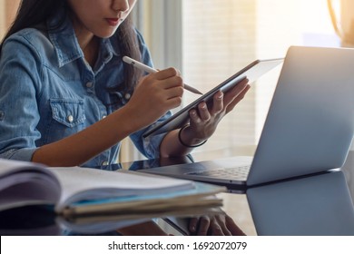 Young asian woman hand holding and using digital tablet, work on laptop computer with book on the desk at home. Online learning, home school concept. - Powered by Shutterstock