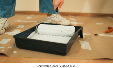 Young Asian woman hand prepare to repair painting wall to renovate redecorate the house living room. Closeup worker hand holding paint roller bush dip into trays container white gray color paint. - Powered by Shutterstock