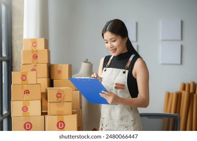 Young asian woman happily prepares orders in her busy office, ensuring smooth delivery for her online shop - Powered by Shutterstock