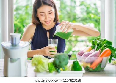 Young Asian Woman Happy Drinking Fresh Green Detox Vegetable Juice. Healthy detox vegan diet with vegetable cold pressed extractor to extract nutrients for smoothie drink. Green healthy food concept.