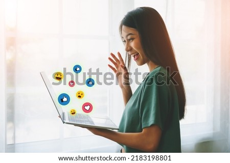 Young asian woman happy smiling and using computer laptop with icon social media and social network beside window