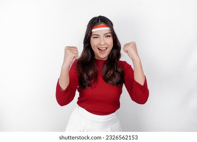 A young Asian woman with a happy successful expression wearing red top and flag headband isolated by white background. Indonesia's independence day concept.
