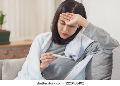 Young Asian woman have a cold and high fever while checking body temperature by using digital thermometer. - Shutterstock ID 1220488402