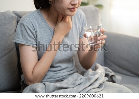 Young Asian woman have a sore throat cough symptom and feel sick from virus or bacteria infection influenza by touching her neck and hard to swallow and drink water