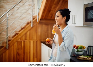 Young Asian woman having a glass of orange juice in the morning at home.  - Powered by Shutterstock
