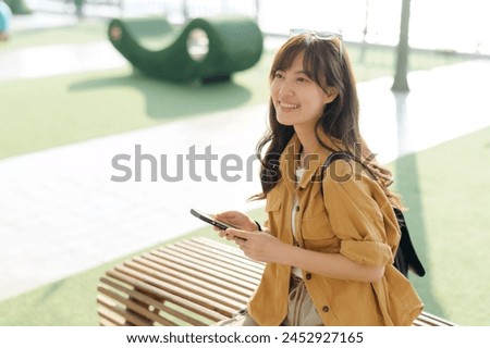 young Asian woman in her 30s, phone in hand, explores a public platform. This portrait embodies the spirit of connected solo travel and cultural discovery.