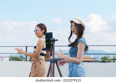 Young Asian woman with her friend er created her dancing video by smartphone camera together on rooftop outdoor at sunset To share video to social media application - Powered by Shutterstock