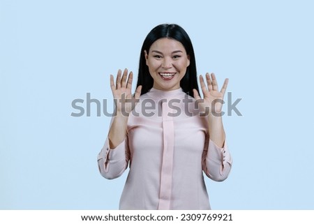 Young asian woman with her hands up shows her palms. Give up gesture. Isolated on pale blue background.