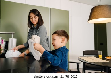 Young asian woman and her little son washing dishes together after dinner in kitchen
