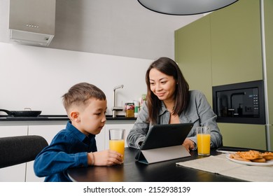 Young asian woman and her little son sitting at table while having breakfast together at home - Powered by Shutterstock