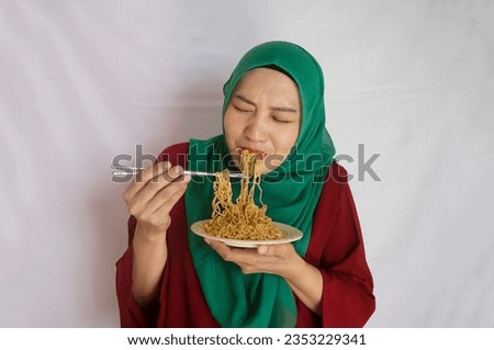 Young Asian woman in hijab eats spicy hot noodle and hanging on chopstick to mouth with sweat delicious enjoy eating