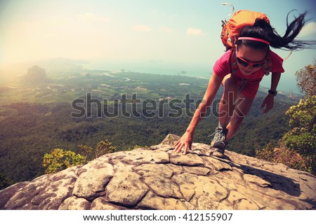 Young asian woman hiker climbing rock at mountain peak cliff edge