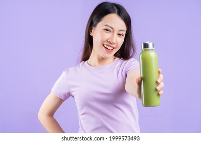 Young Asian woman holding a bottle of juice on purple background