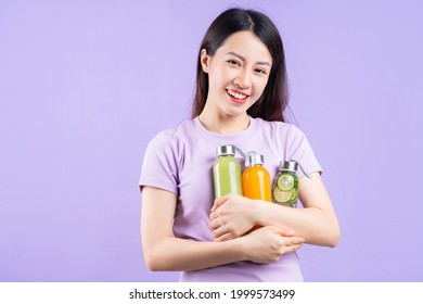 Young Asian Woman Holding A Bottle Of Juice On Purple Background