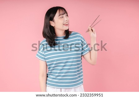 Young Asian woman holding chopsticks isolated on pink background.