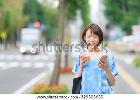Young Asian woman holding a coffee cup and a smart phone.