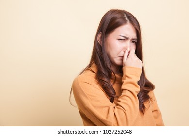 Young Asian woman  holding her nose because of a bad smell on beige background