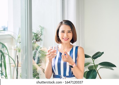 Young Asian Woman Holding Medicine And Water Glass Behind The Window.