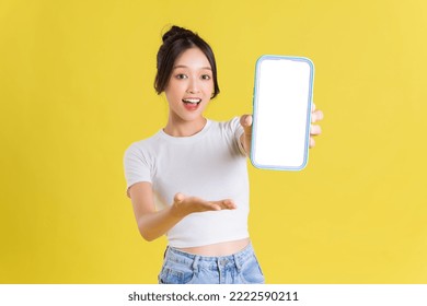 Young Asian woman holding phone with cheerful face on yellow background
