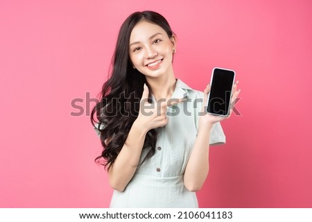 Young Asian woman holding phone in hand and pointing at it with playful expression	