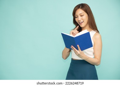 Young asian woman holding and reading a blue book with a smile and her hand posed isolated on green background - Shutterstock ID 2226248719