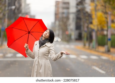 Young Asian Woman Holding Up Red Umbrella In Autumn City.