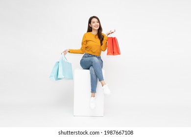 Young Asian Woman Holding Shopping Bags And Sitting On White Box Isolated On White Background