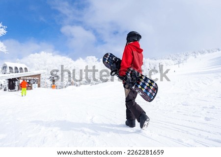 Young Asian woman holding snowboard walking on snowy mountain at in ski resort. Attractive girl enjoy outdoor active lifestyle extreme sport training freeride snowboarding on winter holiday vacation.