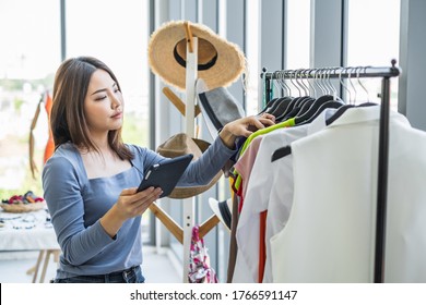 Young Asian woman holding a tablet and checking cloth on a hanging rack in a clothing shop. - Powered by Shutterstock