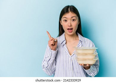 Young Asian Woman Holding Tupperware Isolated On Blue Background Pointing To The Side