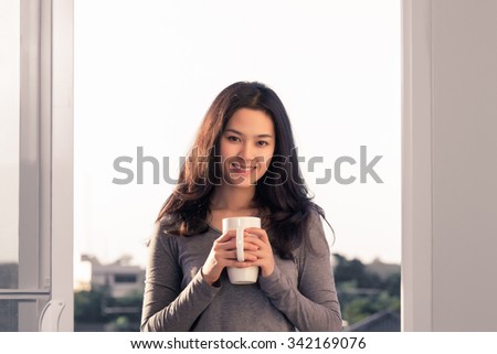 Young Asian woman Holding white mug in balcony.