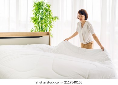 Young asian woman housewife clean bed and set up changing bedsheet with white clean sheet tidy up bedroom.room service and cleaning concept