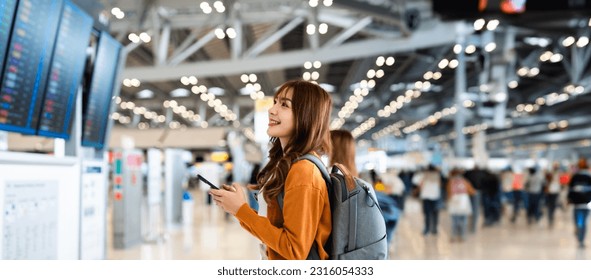 Young asian woman in international airport, using mobile smartphone and checking flight at the flight information board - Shutterstock ID 2316054333