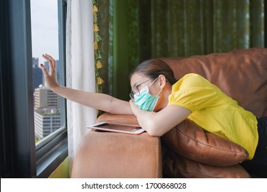 Young Asian Woman Isolating At Home With Tablet On The Sofa In The Living Room. She Is Bored Because Stay At Home Campaign For Coronavirus Prevention.