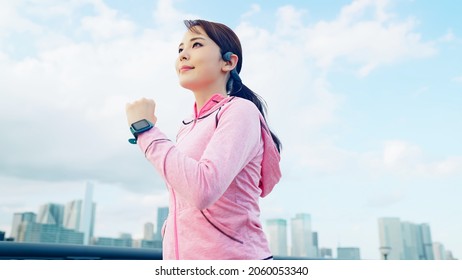Young Asian woman jogging in front of the city. - Shutterstock ID 2060053340