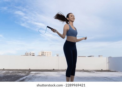 Young Asian woman with jump rope on rooftop. Fitness female doing skipping workout outdoors  - Powered by Shutterstock