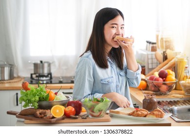 Young Asian Woman In The Kitchen Prepare And Eating Sandwich For Breakfast