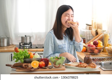 Young Asian Woman In The Kitchen Prepare And Eating Sandwich For Breakfast