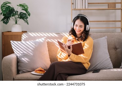 Young Asian woman listening music from headphones and eating dessert during read her book.She in home office or cafe